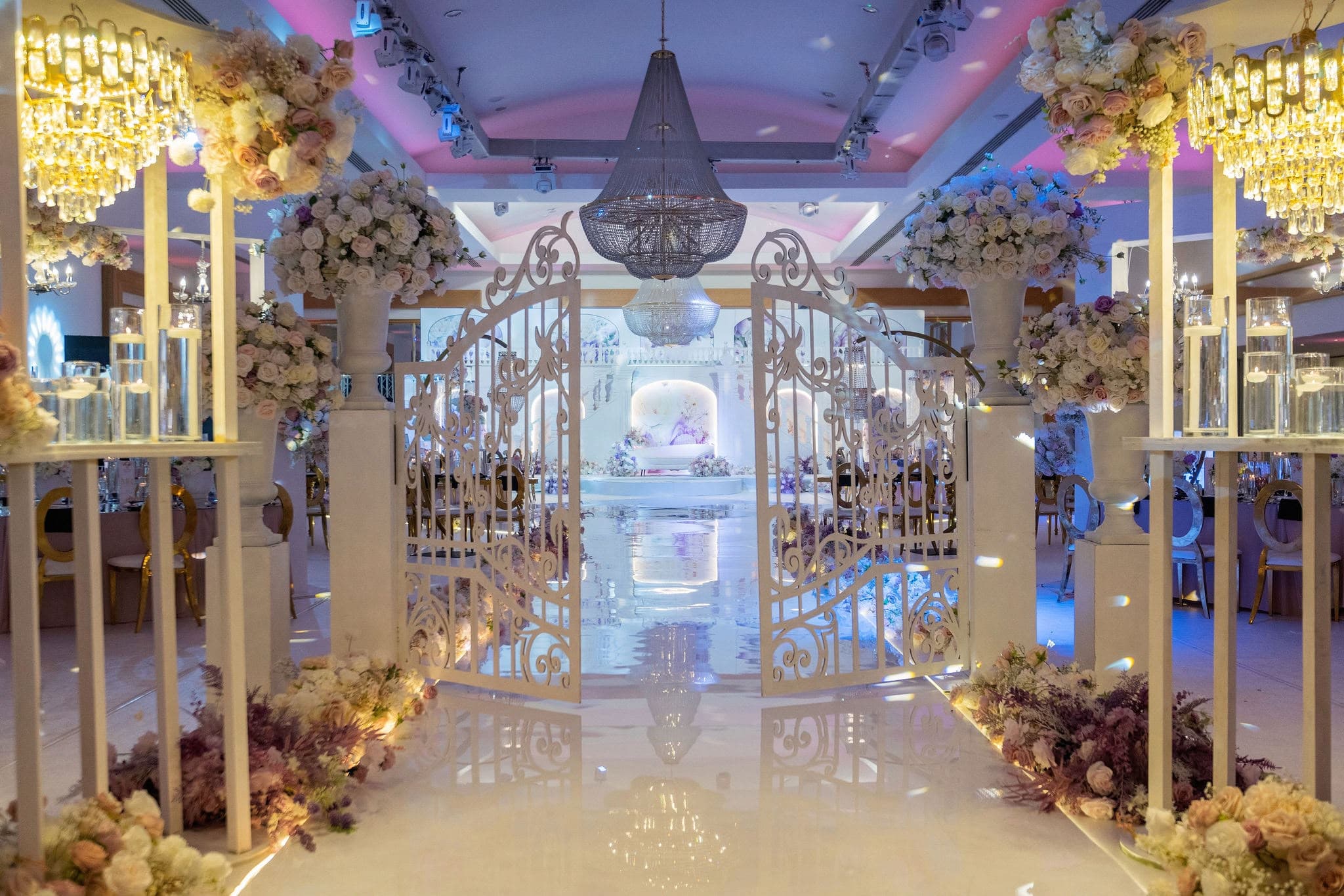 Gold candle stands framing the entrance to a chandelier-lit wedding