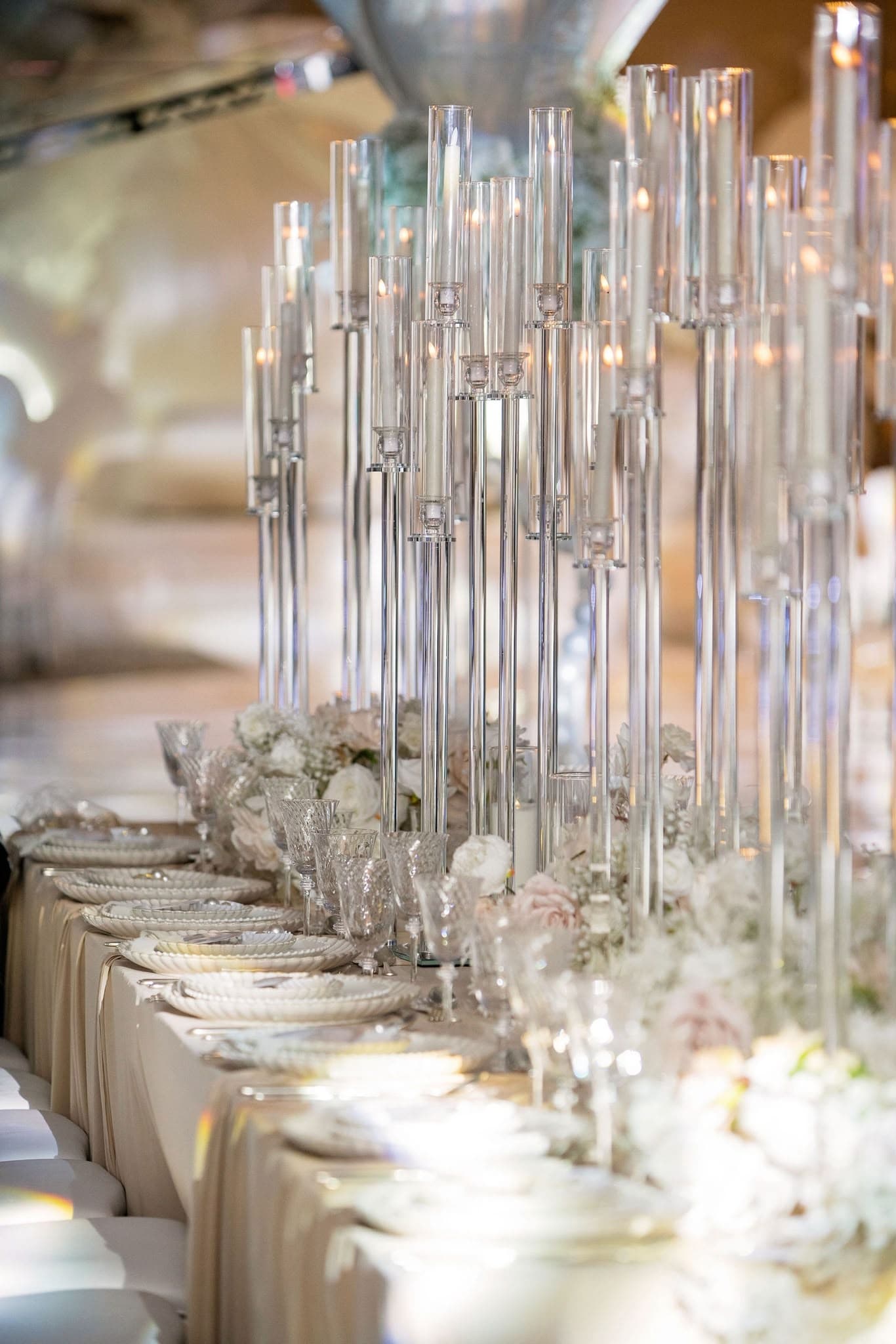 Tall crystal candleholders above white flowers and gold table settings