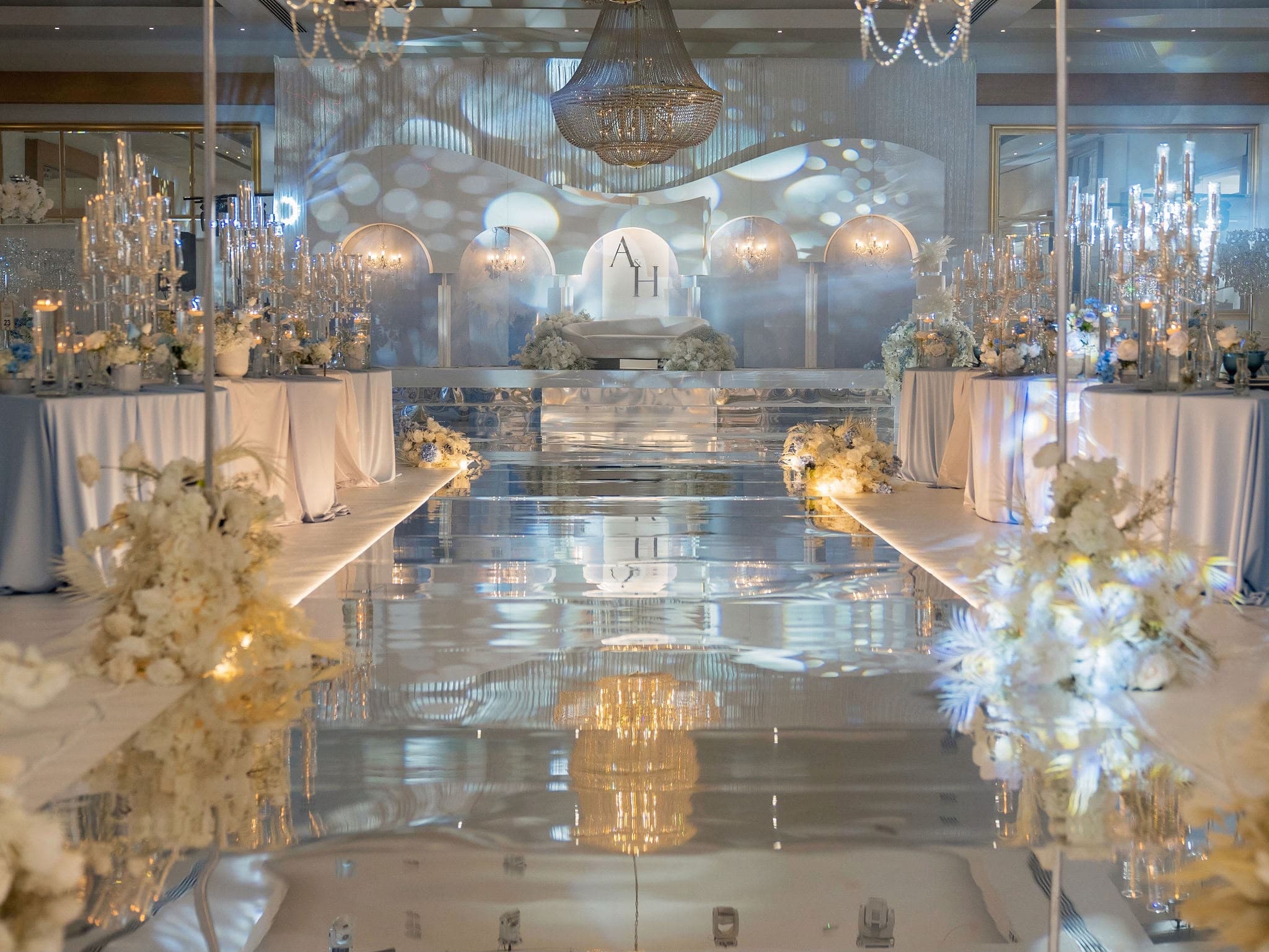 Crystal chandeliers reflected in a mirrored aisle at a blue and gold reception