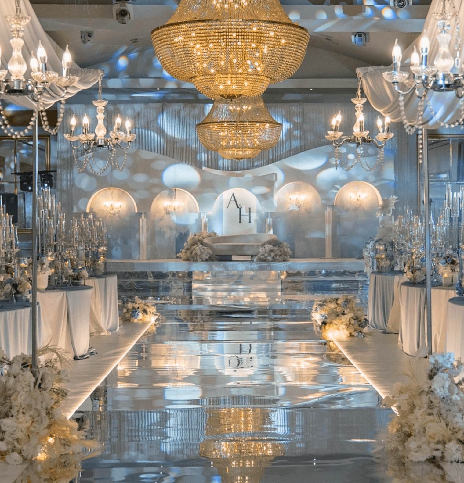 Crystal chandeliers above a mirrored wedding aisle lined with white flowers